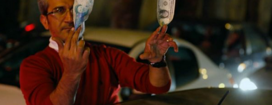 مواطن إيراني يحمل العملتين الإيرانية والأمريكية